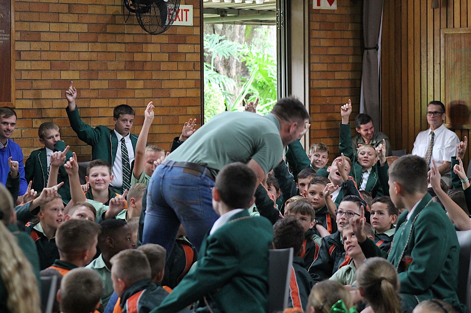 Learners raising hands as Jaco Kriel engages them in the school hall
