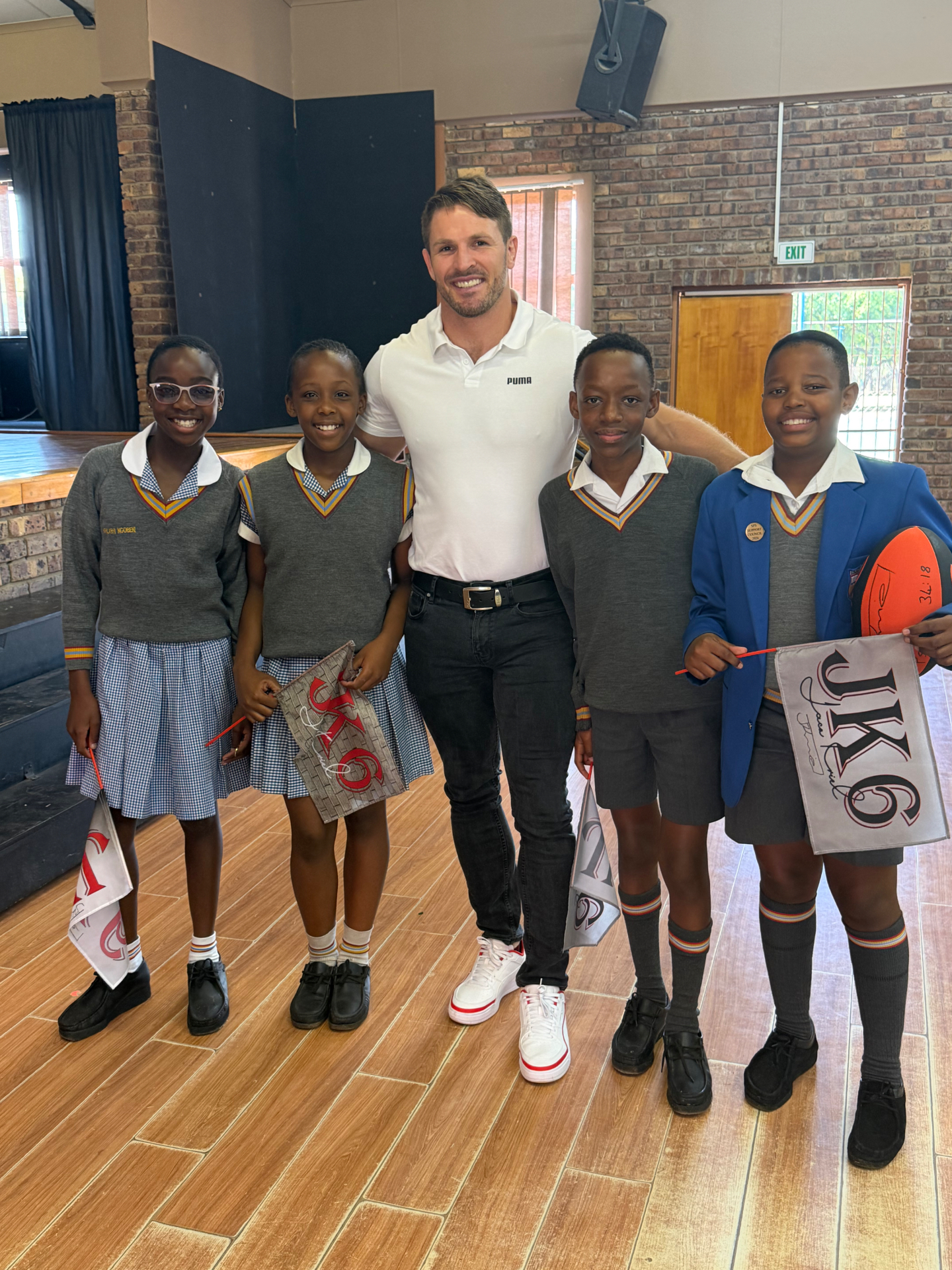 Jaco Kriel with four learners holding signed JK6 flags and a signed rugby ball