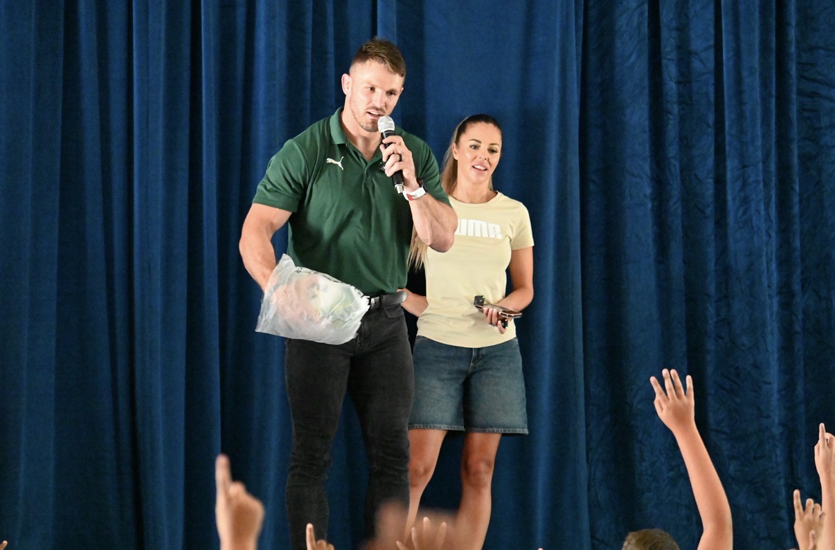 Jaco Kriel on stage with a microphone and prize bag as learners raise their hands