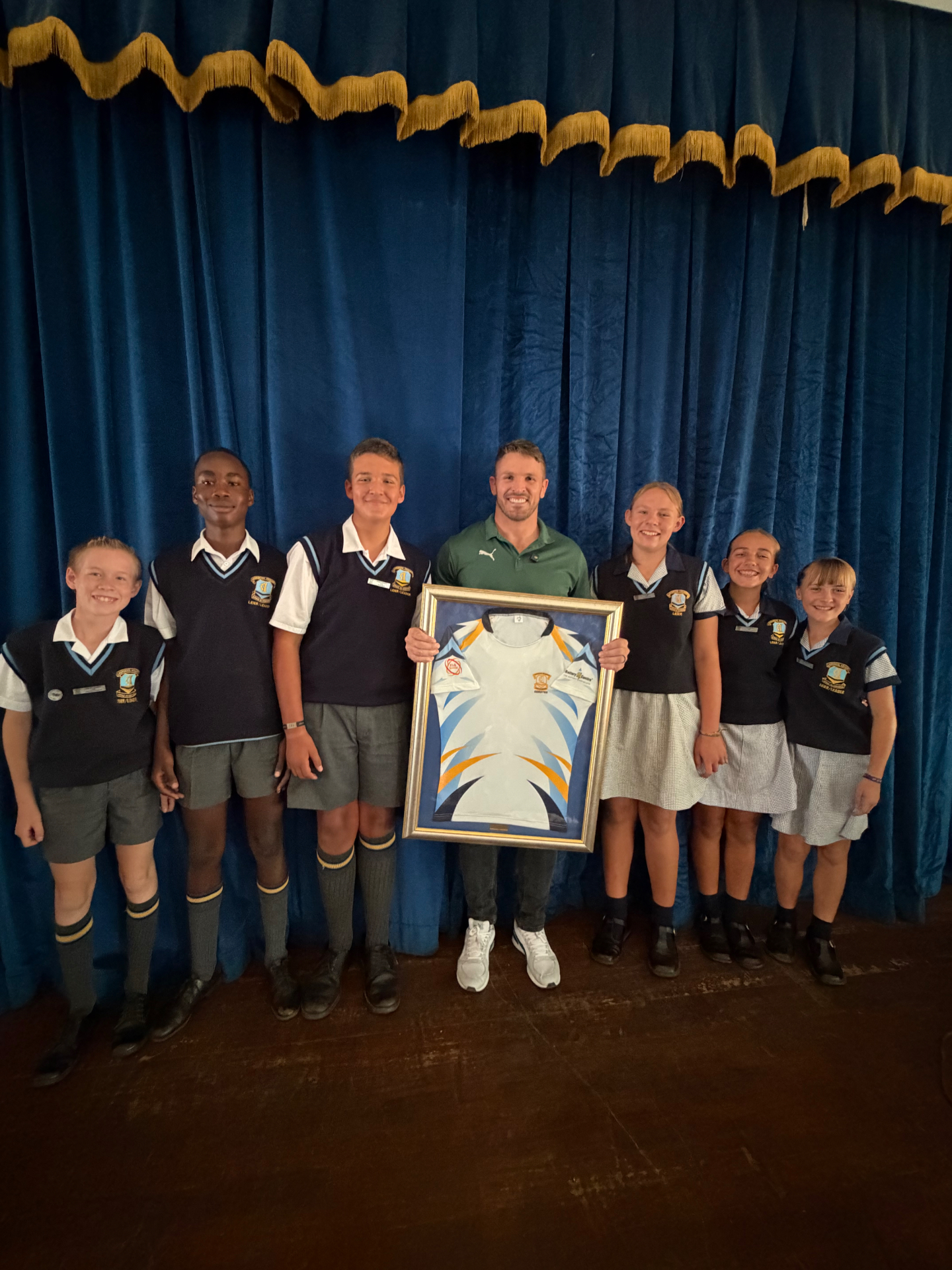 Jaco Kriel on stage with school prefects holding a framed signed jersey