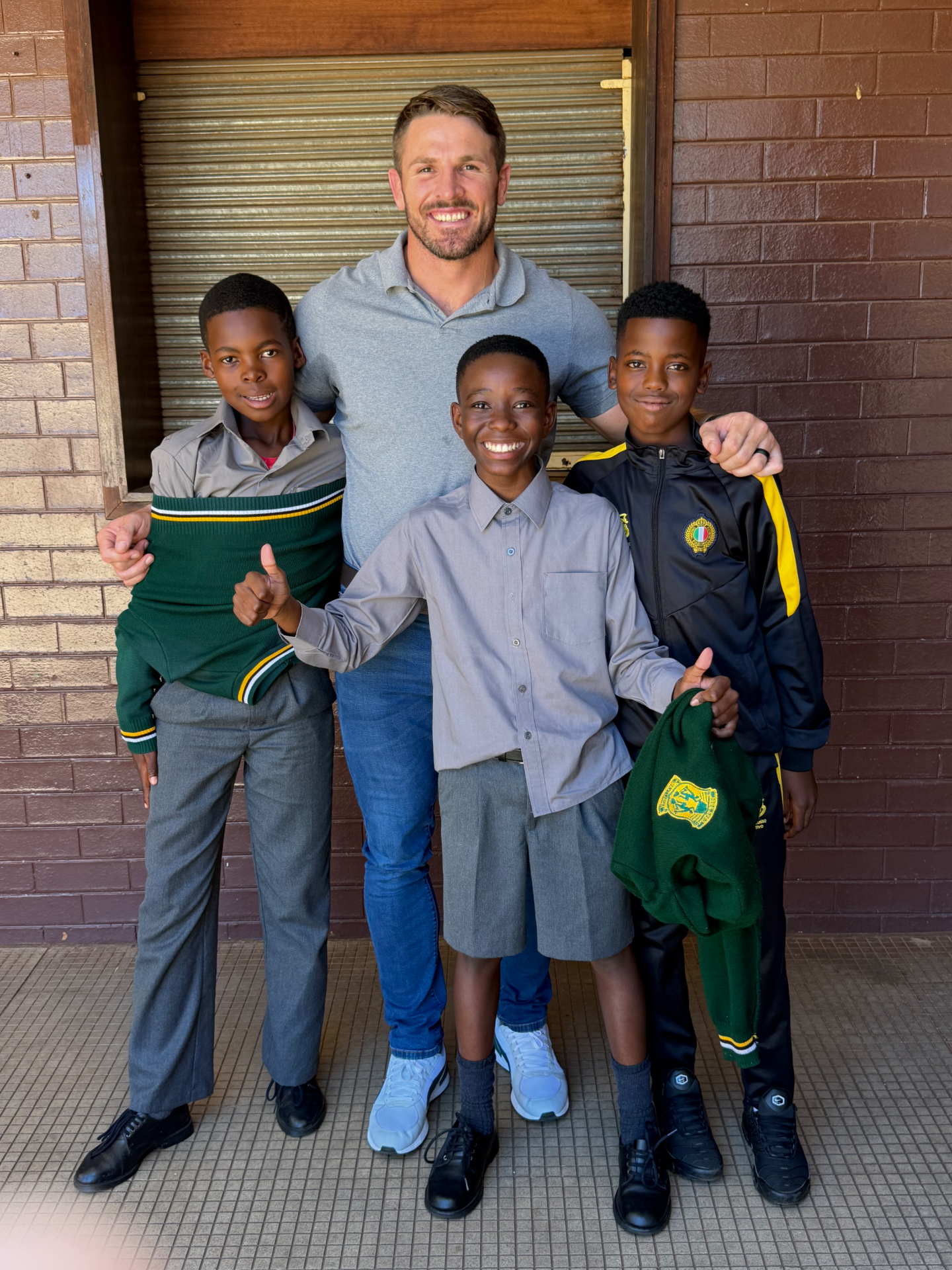 Jaco Kriel with three smiling school boys giving thumbs up after a JK6 school visit