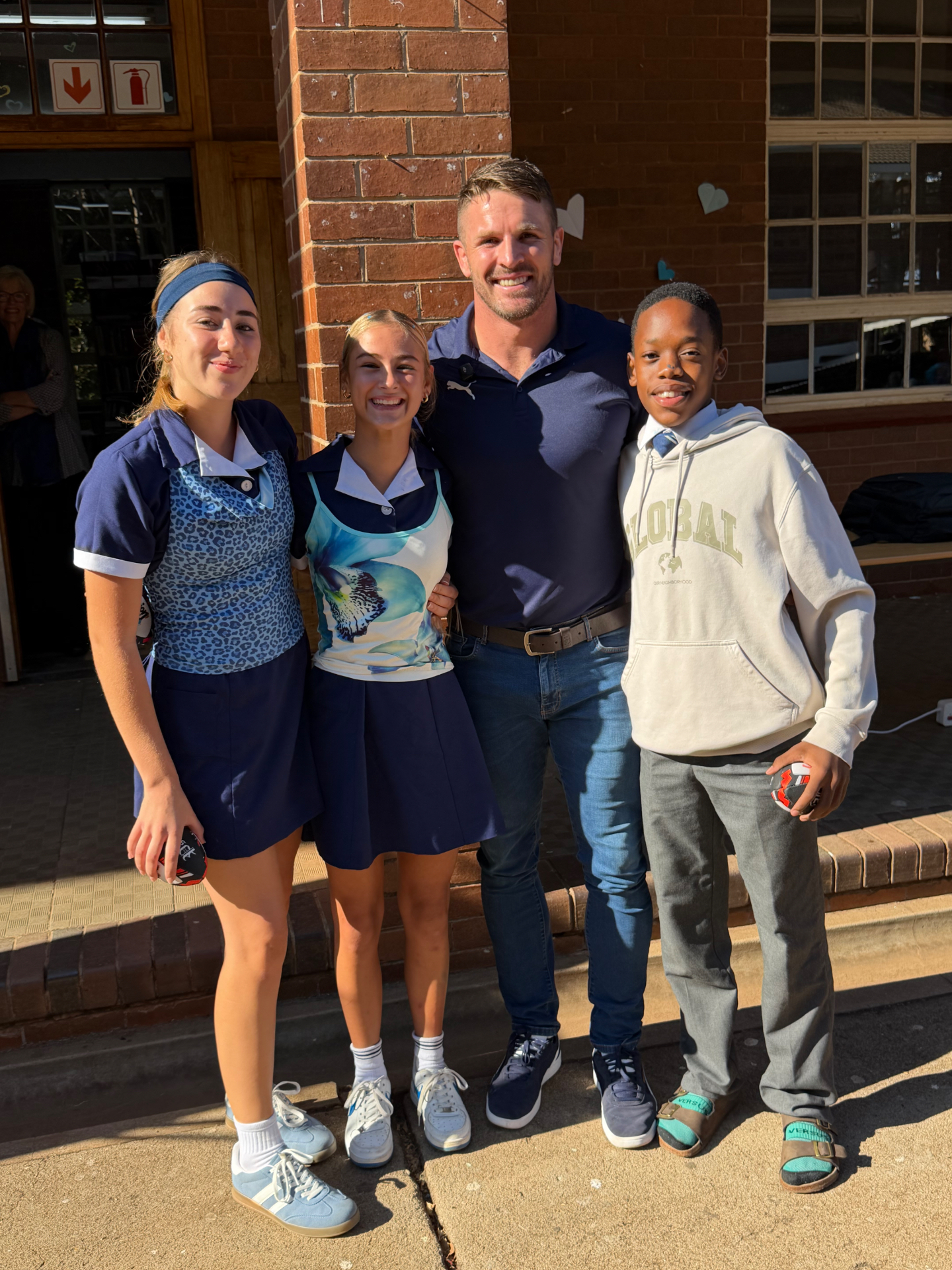 Jaco Kriel with three smiling learners holding JK6 rugby balls at a school visit
